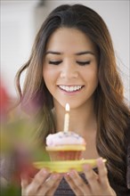 Hispanic woman blowing out cupcake candle