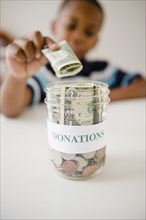 Black boy putting money into donations jar