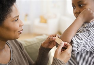Black mother putting bandage on son's elbow