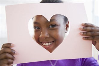 Black girl looking through heart-shaped opening in paper