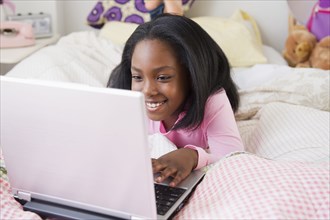 Black girl laying on bed using laptop