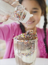 Mixed race girl putting sprinkles on ice cream