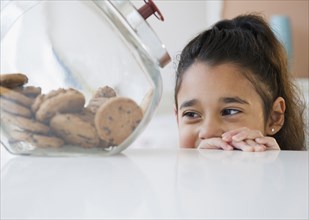 Mixed race girl looking at cookies in cookie jar