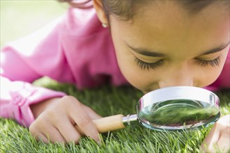 Mixed race girl looking at grass with magnifying glass