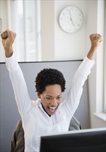 African American businesswoman sitting at desk cheering