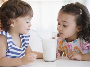 Mixed race sisters sharing glass of milk