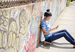 Asian woman sitting on skateboard using cell phone