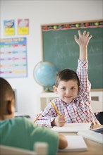 Caucasian boy raising hand in classroom