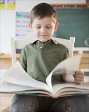 Caucasian boy reading book in classroom