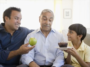 Hispanic father and son offering grandfather apple and cupcake