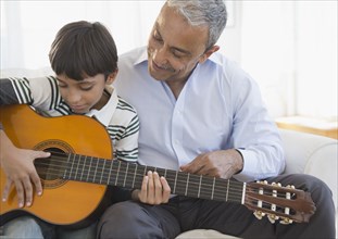 Hispanic grandfather watching grandson playing guitar