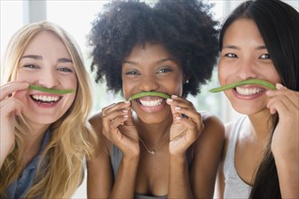 Smiling women using green beans as mustaches
