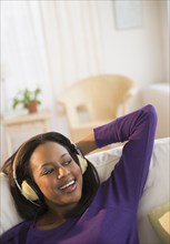 African American woman listening to headphones on sofa