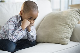 Sulking African American boy sitting on sofa