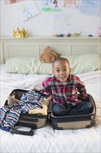African American boy sitting in suitcase on bed