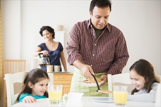 Father serving daughters breakfast at table