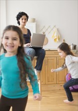 Mother using laptop as daughters play