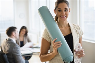 Businesswoman holding yoga mat in office