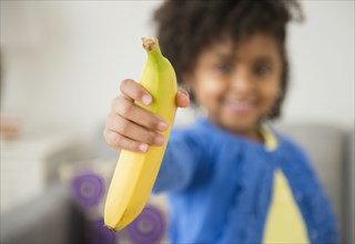 African American girl holding banana on sofa