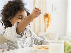 African American girl eating plate of spaghetti