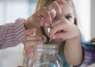 Girls putting coins in savings jar