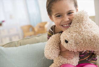 Hispanic girl hugging teddy bear on sofa