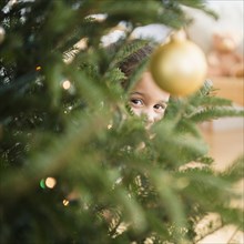 Hispanic girl peeking behind Christmas tree