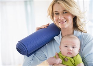 Caucasian mother with baby holding yoga mat