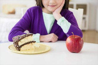 Mixed race girl choosing between cake and apple