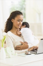 Hispanic mother using laptop and holding infant son