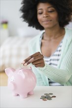 Mixed race woman putting coins in piggy bank