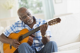 Black man playing guitar on sofa