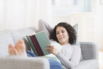 Mixed race woman reading on sofa