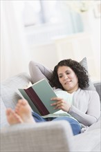 Hispanic woman reading on sofa