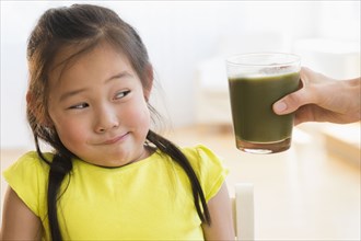 Korean girl frowning at glass of green smoothie