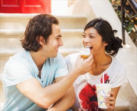 Man feeding donut to girlfriend on front stoop
