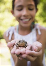 Mixed race girl holding frog outdoors