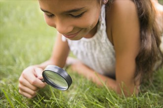 Mixed race girl using magnifying glass in grass