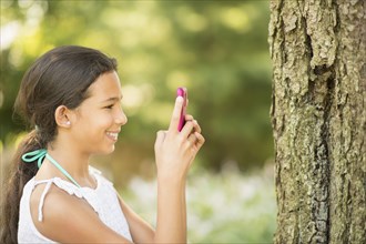 Mixed race girl photographing tree trunk with camera phone