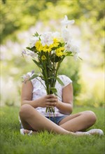 Mixed race girl holding bouquet of flowers in grass