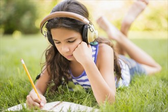 Mixed race girl listening to headphones and drawing in grass