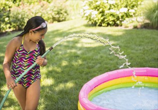 Mixed race girl filling wading pool in backyard