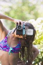 Mixed race girl taking pictures with toy camera outdoors