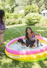 Mixed race girls playing with dog in wading pool