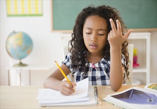 Mixed race student counting on fingers in classroom