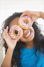 Mixed race girl holding donuts over her eyes
