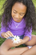 Mixed race girl picking petals off daisy