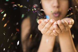 Close up of Asian woman blowing confetti from hands