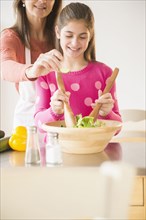 Caucasian mother and daughter tossing salad in kitchen