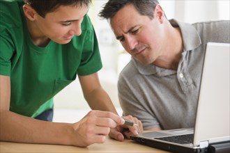 Caucasian son showing father how to use USB stick in laptop